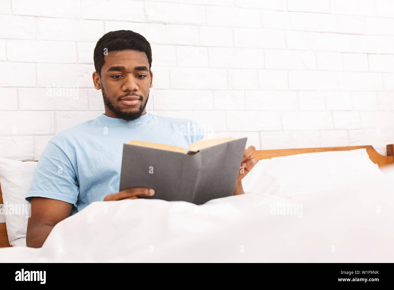 Nachdenklicher junger Mann lesen Buch im Bett Stockfoto