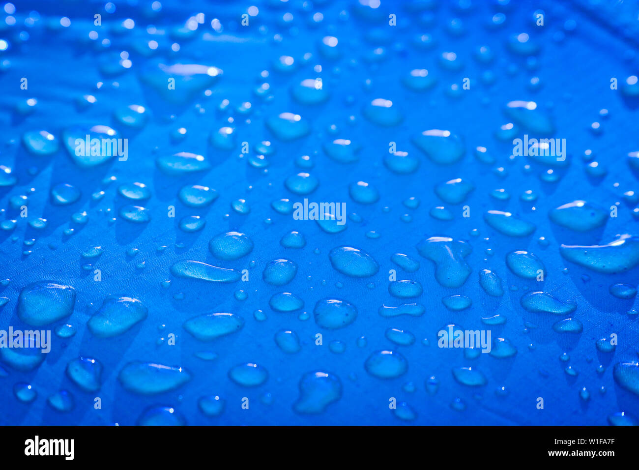 Große Tropfen von Wasser auf einer Blau Textil mit einer wasserdichten Effekt. Wasserabweisende Imprägnierung. Textur Tropfen auf das Gewebe. Stockfoto