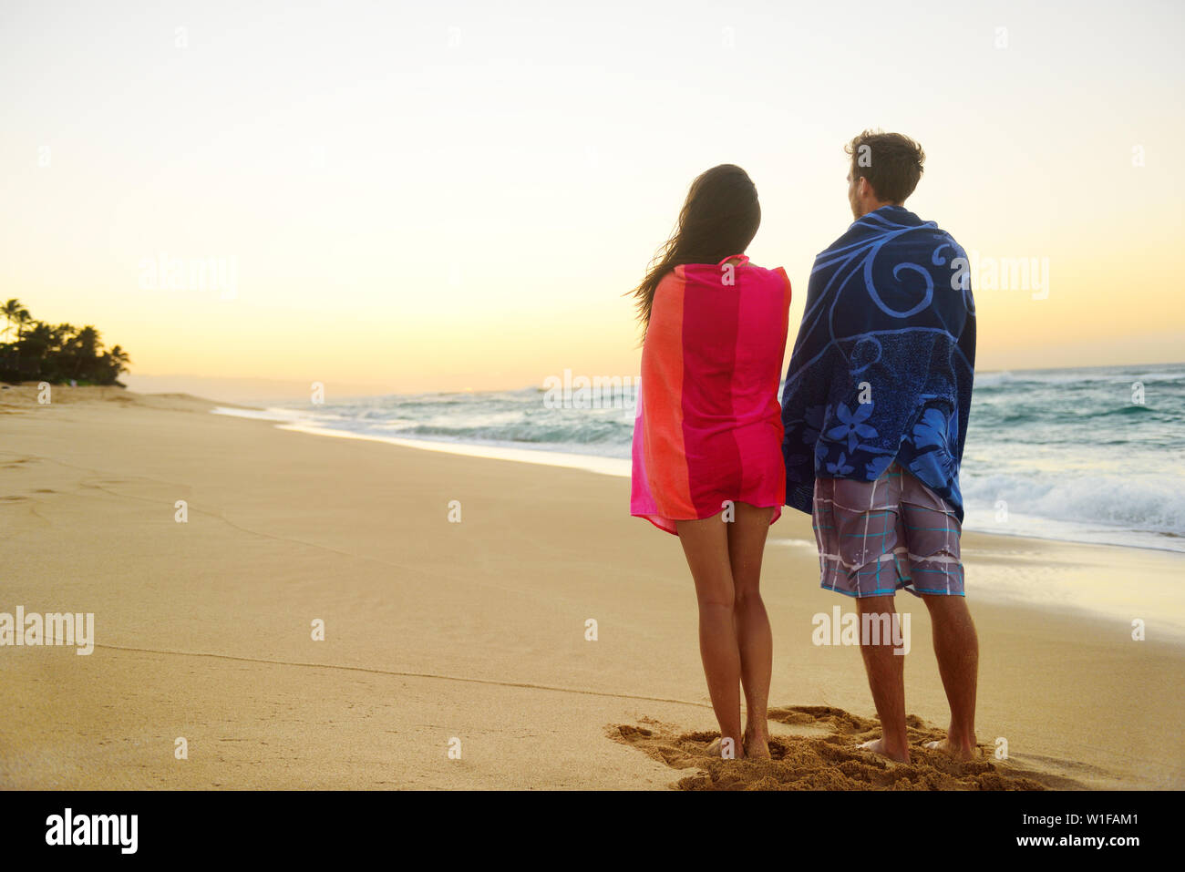 Paar stehend in Strand sand, Handtücher über die Schultern genießen Ozean Sonnenuntergang während Reisen Urlaub Wochenende Urlaub. Mixed Race Paar, asiatische Frau, kaukasische Mann. Stockfoto