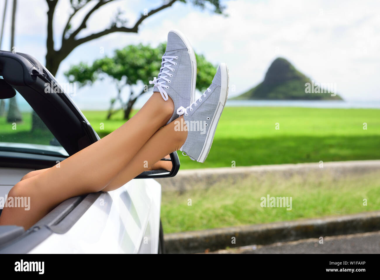 Entspannender Urlaub Autofahrt mit den Füßen zum Fenster. Cabrio-Urlaubskonzept mit weiblichen Beinen vor dem Wahrzeichen von Oahu: Mokoli'i Island (früher bekannt als der veraltete Begriff "Chinaman's hat") in Hawaii, USA. Stockfoto