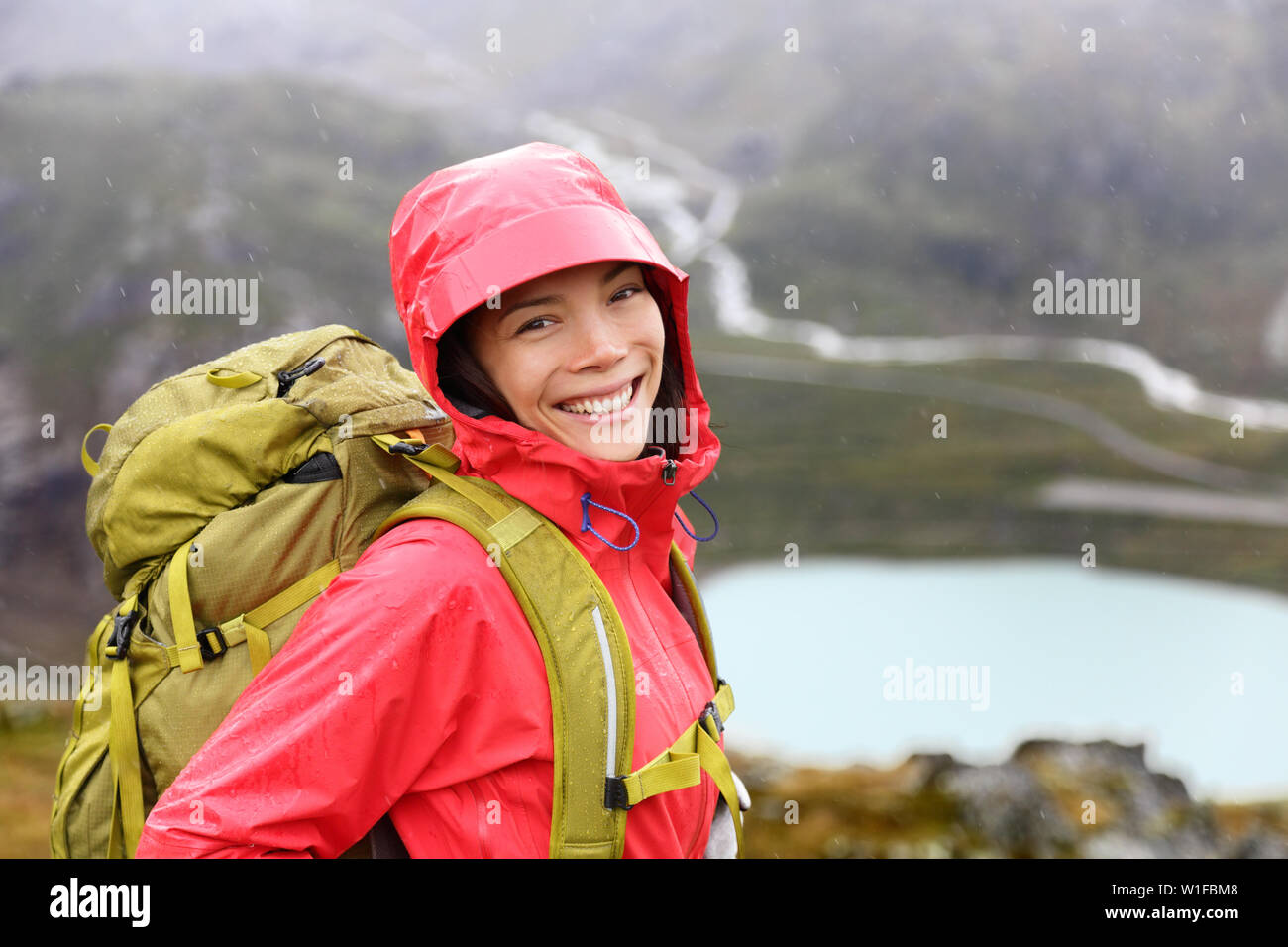 Wanderer Frau wandern mit Rucksack im Regen auf Trek Leben gesundes Leben. Lächelnd frischen und ehrlichen jungen asiatischen Mädchen zu Fuß auf Wanderung in die Berge Natur Landschaft während in den Schweizer Alpen regnet, Schweiz. Stockfoto