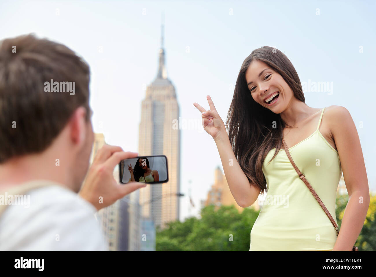 NYC asiatische chinesische Touristen Mädchen am Empire State Building posiert die v Handzeichen. Junge paar Touristen fotografieren mit Smartphone in New York City vor der berühmten Wahrzeichen. Stockfoto