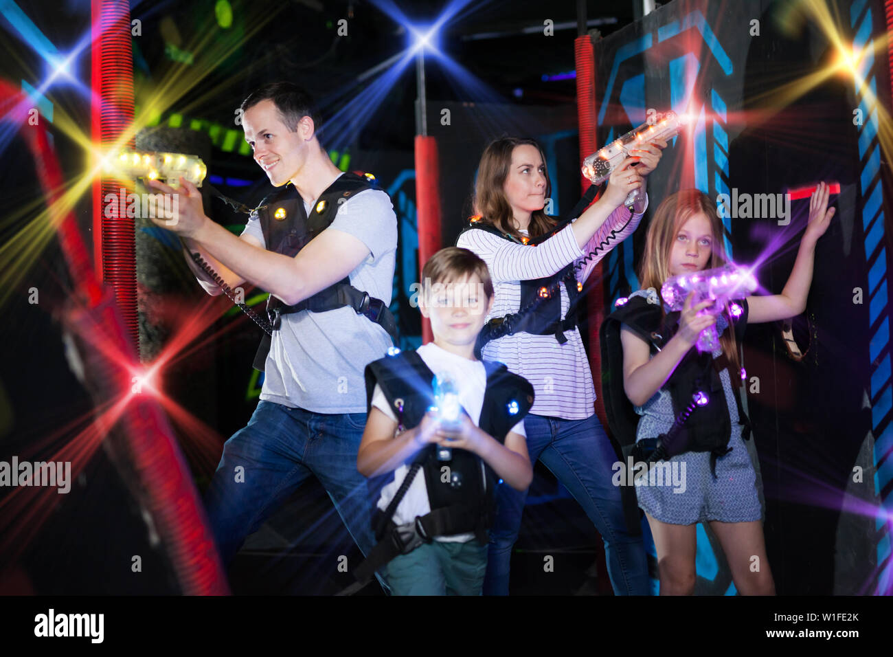 Moderne junge Eltern und Kinder spielen Laser tag in dunklen Labyrinth ...