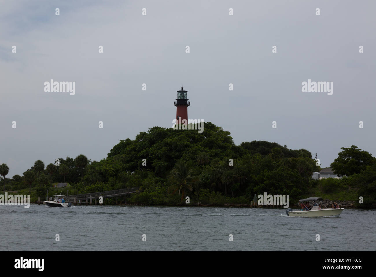Boote Reisen die Loxahatchee River unterhalb der historischen Jupiter Inlet Leuchtturm unter einem bewölkten Südflorida Himmel. Stockfoto