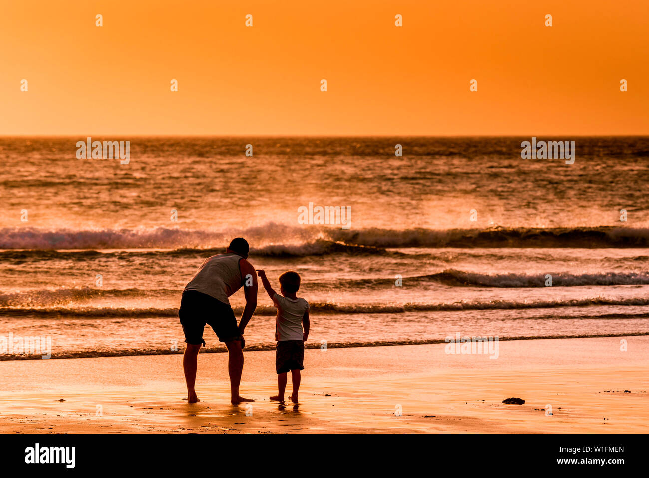 Ein Vater und sein Sohn genießen den wunderschönen Sonnenuntergang über den Fistral Beach in Newquay in Cornwall. Stockfoto