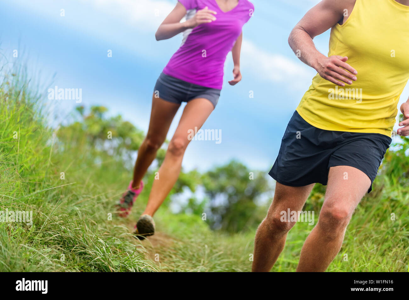 Fitness Sportler Trail Running - athletische Beine closeup untere Körper Ernte von Mann und Frau ausarbeiten. Sport Leute joggen im Zeitraffer Marathon Training auf dem Naturlehrpfad in Shorts Sportbekleidung. Stockfoto