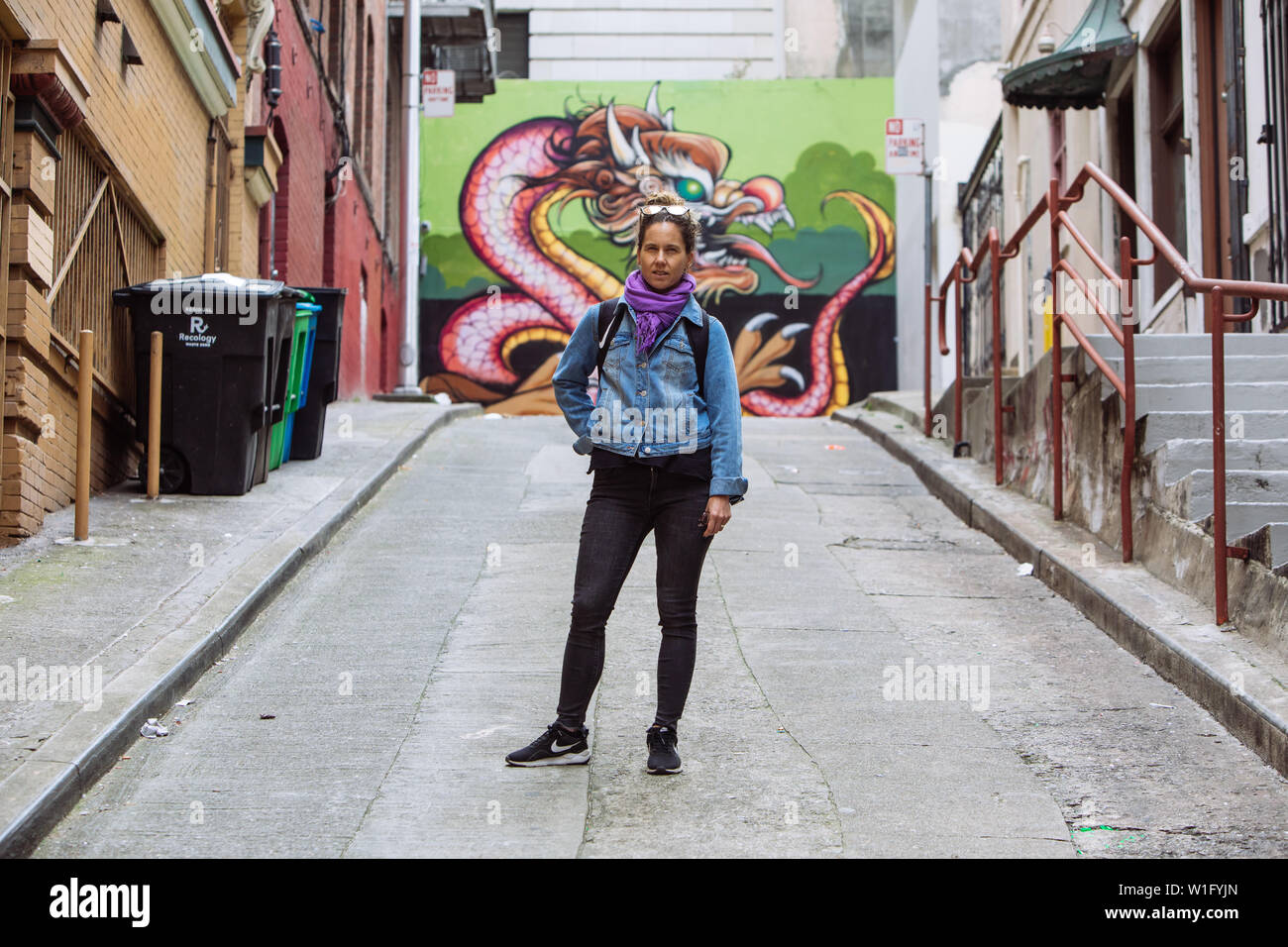 Frau mittleren Alters posiert in einer Gasse mit einem Drachen Graffiti in China Town, San Francisco, Kalifornien, USA Stockfoto