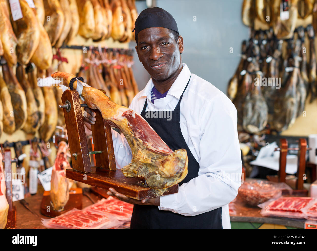 Happy African American Verkäufer in Fleisch shop arbeiten, empfehlen köstliche iberischen Schinken Stockfoto