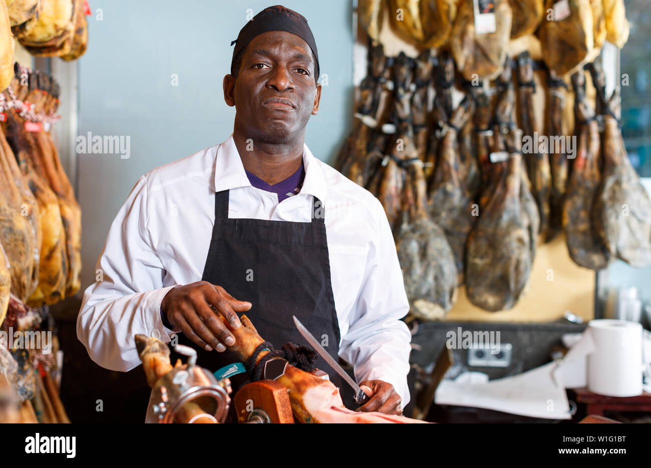 Zuversichtlich Afrikanische amerikanische Verkäufer schneiden köstlichen Schinken zum Verkauf in Metzgerei Stockfoto