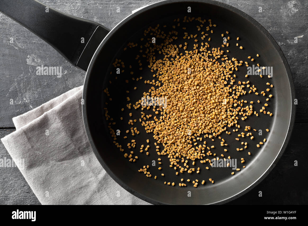 Getrocknet, raw Bockshornklee Samen in eiserne Pfanne zum Braten auf dunklen Moody schwarze Küche Tisch Hintergrund Draufsicht von oben flach legen mit selektiven Fokus Stockfoto