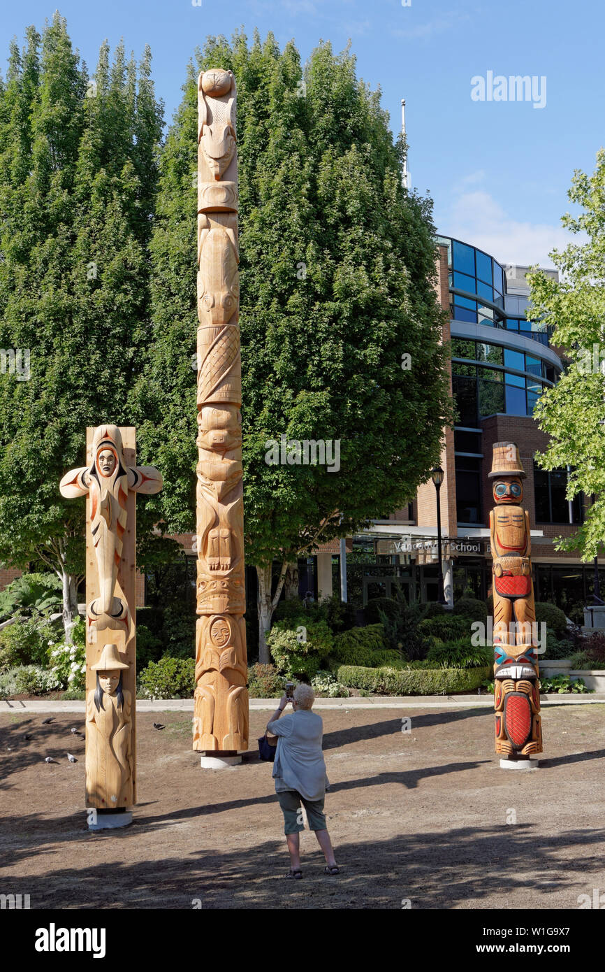 Frau fotografiert Kwakiutl Stil Versöhnung Totem Pol und Willkommen Beiträge außerhalb der Vancouver School Board Gebäude, Vancouver, BC, Kanada Stockfoto