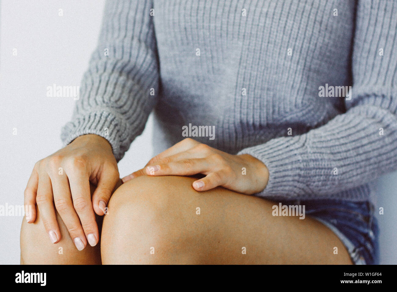 Hände einer jungen Frau auf den Knien, die Hände mit einer ordentlichen Maniküre, eine junge Frau im lässigen Stil Kleidung, ein warmes grau Pullover. Horizontale Farbe Photogra Stockfoto