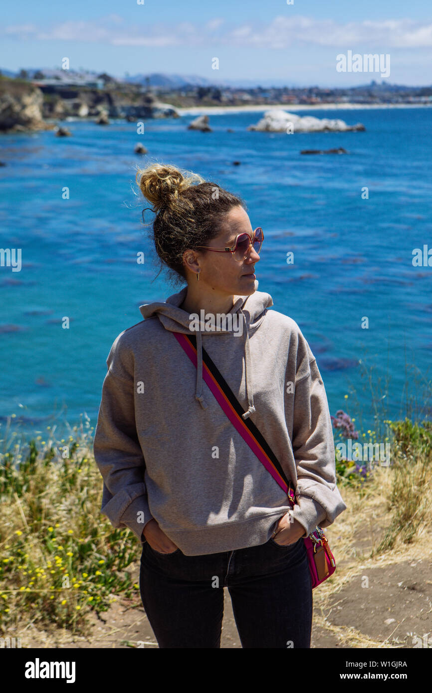 Frau mittleren Alters trägt einen Sport-Hoodie mit Schattierungen, die auf eine Seite blicken, mit Hintergrund von Pismo Beach, San Luis Obispo, Kalifornien, USA Stockfoto