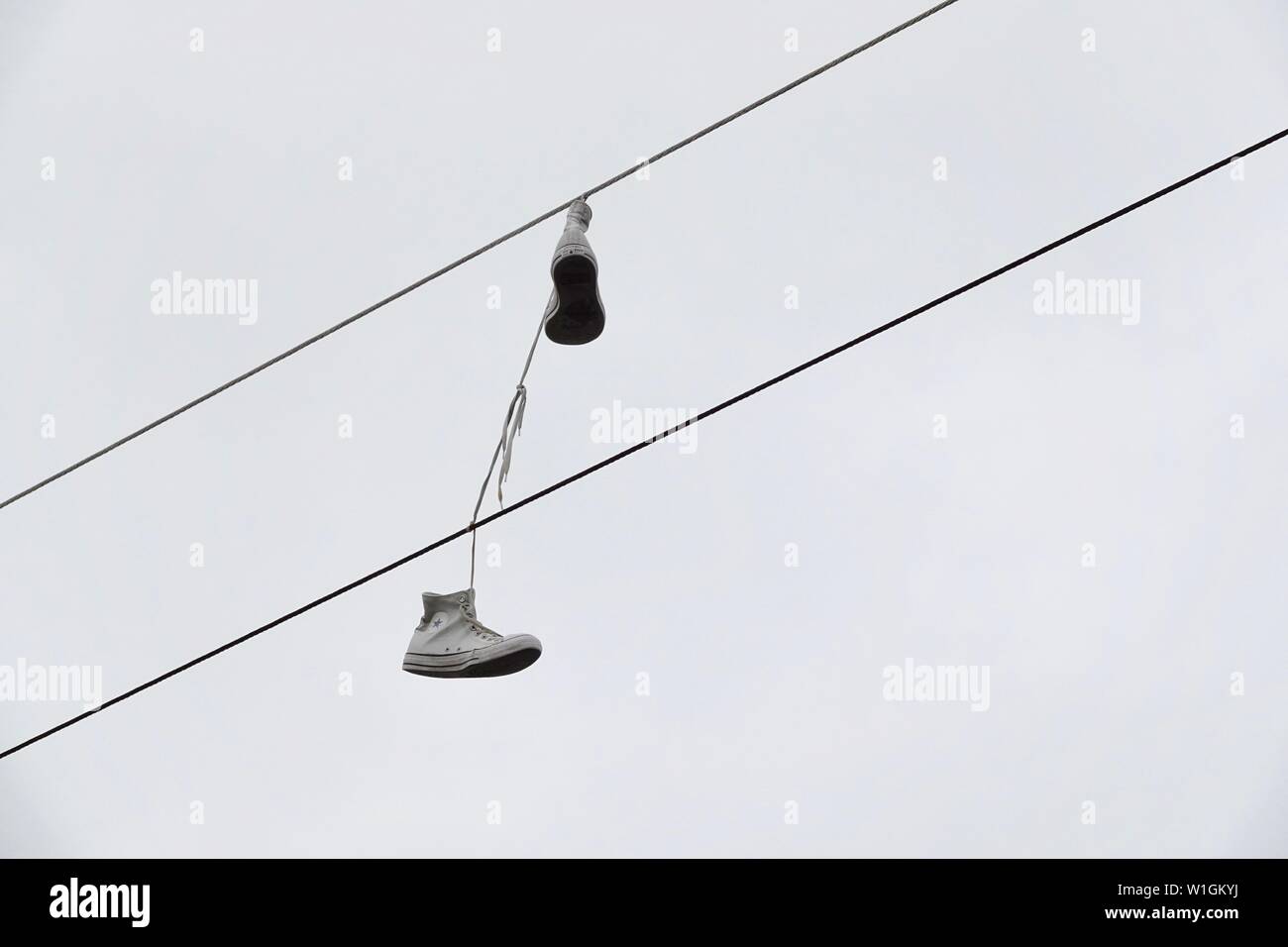 Ein Paar Turnschuhe hängen von einem elektrischen Kabel über eine Straße. Stockfoto