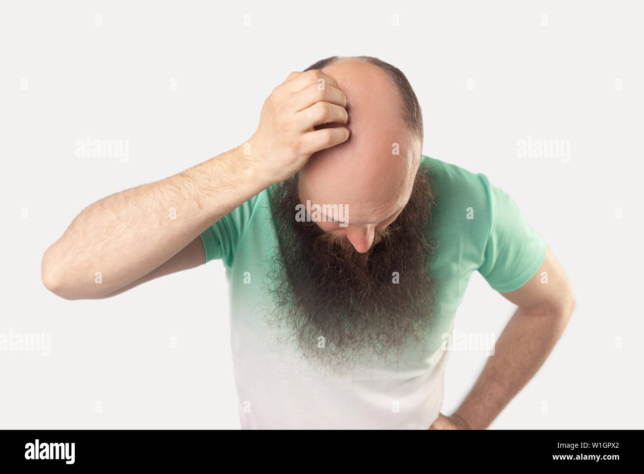 Porträt der glatzköpfige Mann mittleren Alters mit langen Bart in hellem Grün t-shirt stehen und zeigt seine Kahlheit auf seinem Kopf. indoor Studio shot, auf isolierte Stockfoto