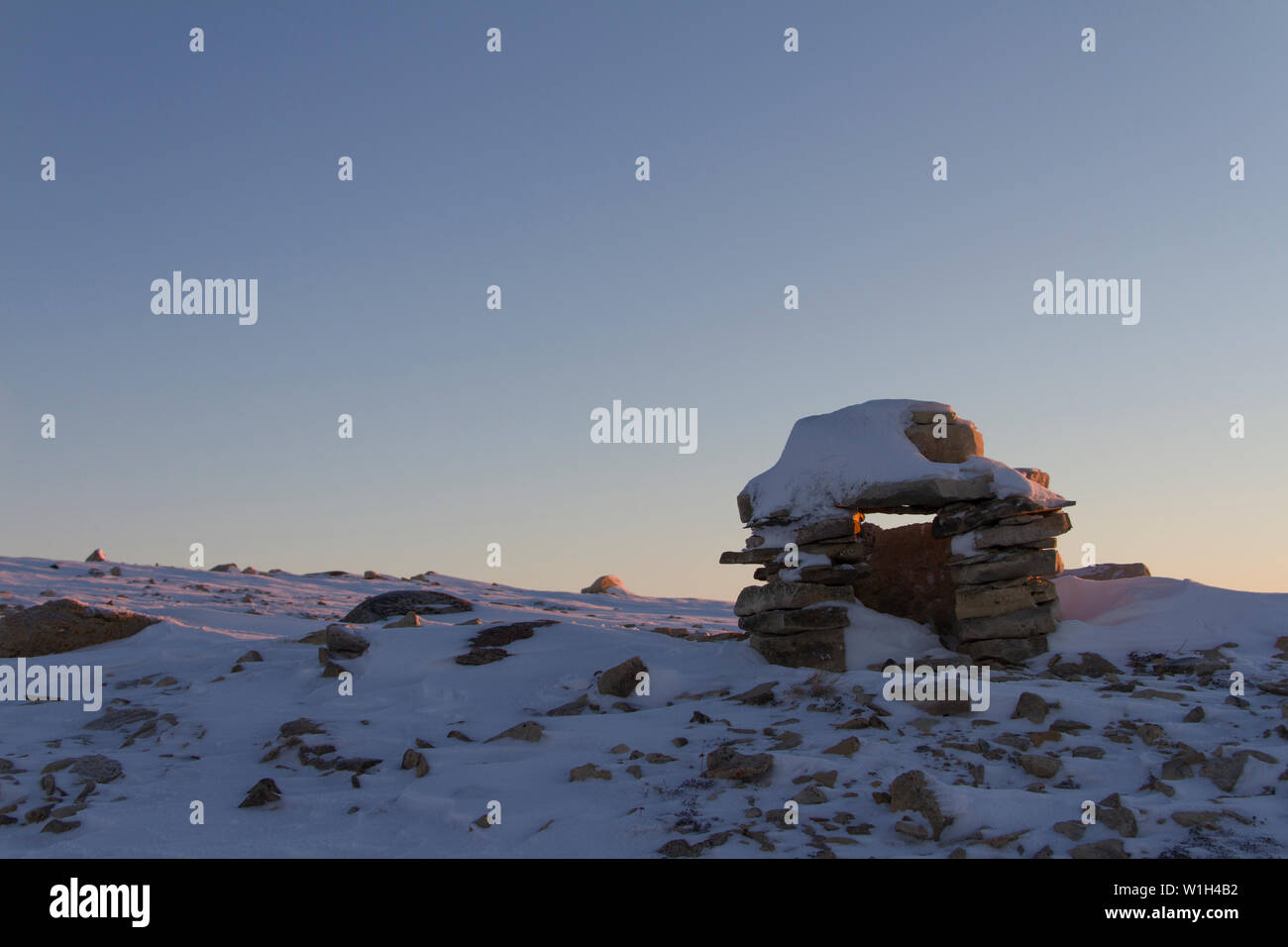 Inuksuk oder Inukshuk Inuit Wahrzeichen bedeckt mit Schnee bei Sonnenaufgang auf einem Hügel in der Nähe der Gemeinde Cambridge Bay, Nunavut, Kanada gefunden Stockfoto