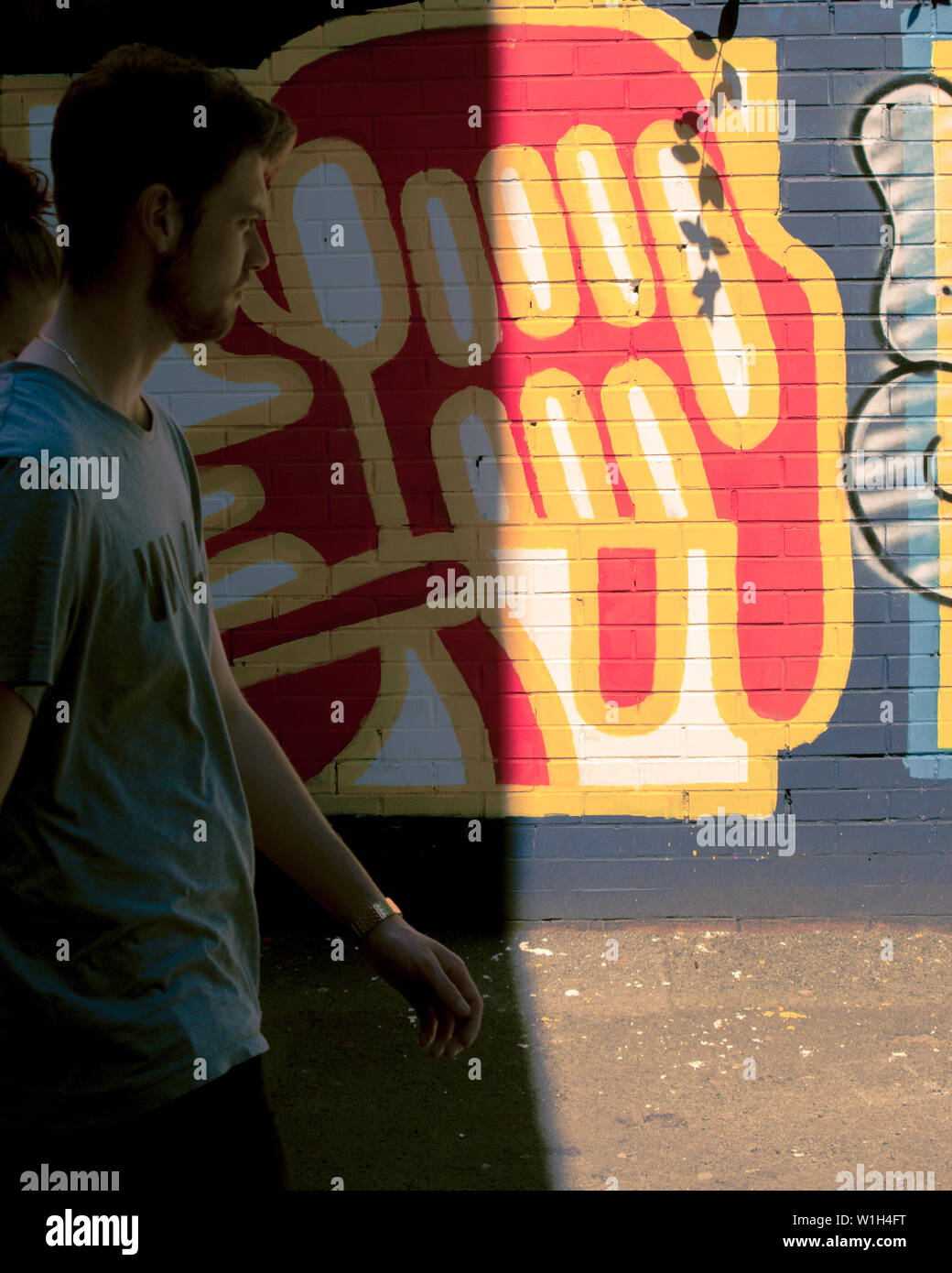 Mann Anfang 30 das Laufen auf den Straßen von Manchester Vergangenheit ein buntes Graffiti an der Wand. Stockfoto
