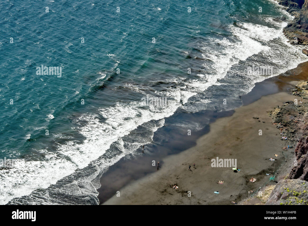 Das türkis-blauen Atlantik mit weißen Wellen in einem diagonalen Schnitt mit einem grauen schönen Strand von weit oben fotografiert. Auf Teneriffa in Igueste de San Stockfoto