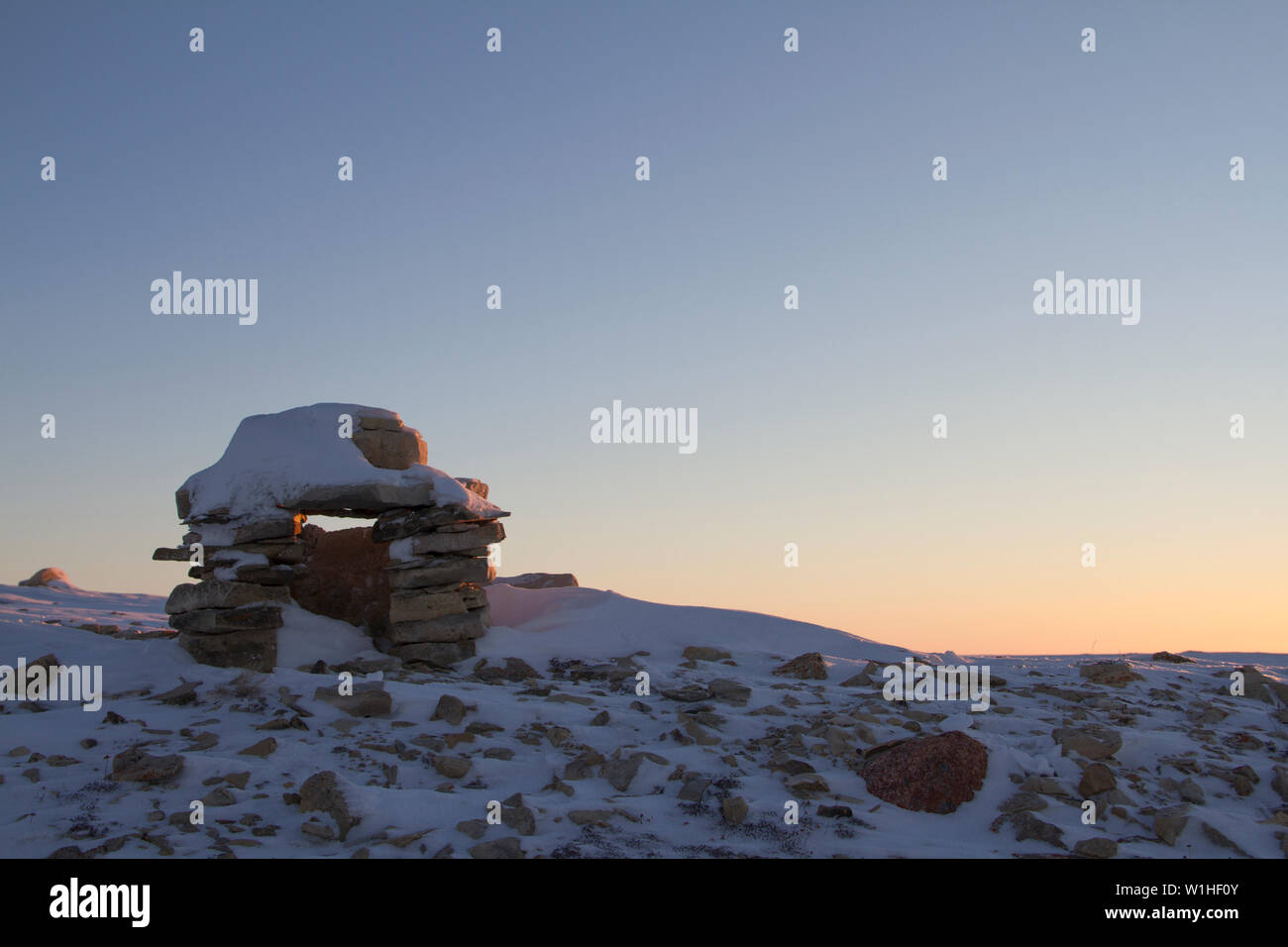 Inuksuk oder Inukshuk Inuit Wahrzeichen bedeckt mit Schnee bei Sonnenaufgang auf einem Hügel in der Nähe der Gemeinde Cambridge Bay, Nunavut, Kanada gefunden Stockfoto