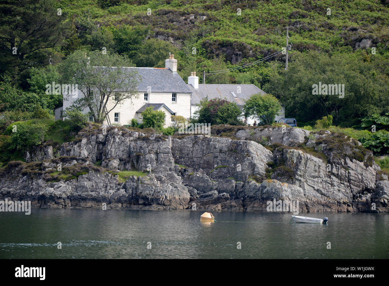 Croft Haus auf Water's Edge von Loch in Schottland. Ein Boot ist in der Nähe der felsigen Ufer vertäut. Stockfoto