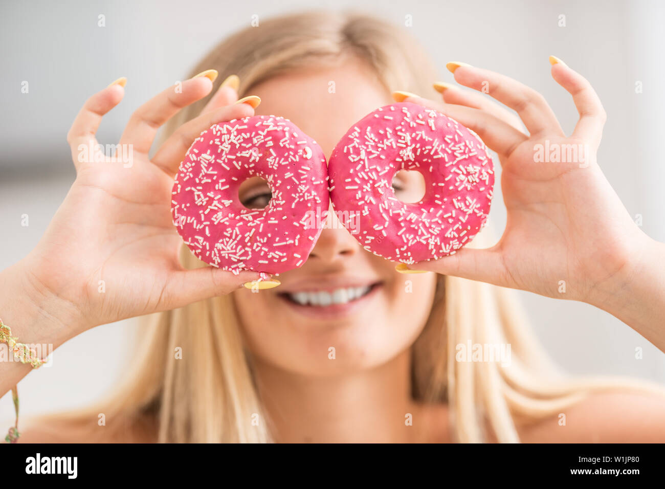 Junge Mädchen bedeckte ihr Gesicht mit rosa Donuts in der Küche zu Hause. Emotion morgen beim Frühstück. Stockfoto