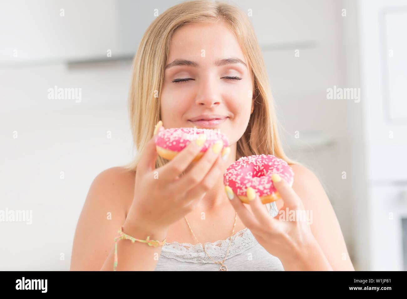 Junge blonde Mädchen isst Rosa donuts Home Küche mit Geschmack Emotionen. Stockfoto