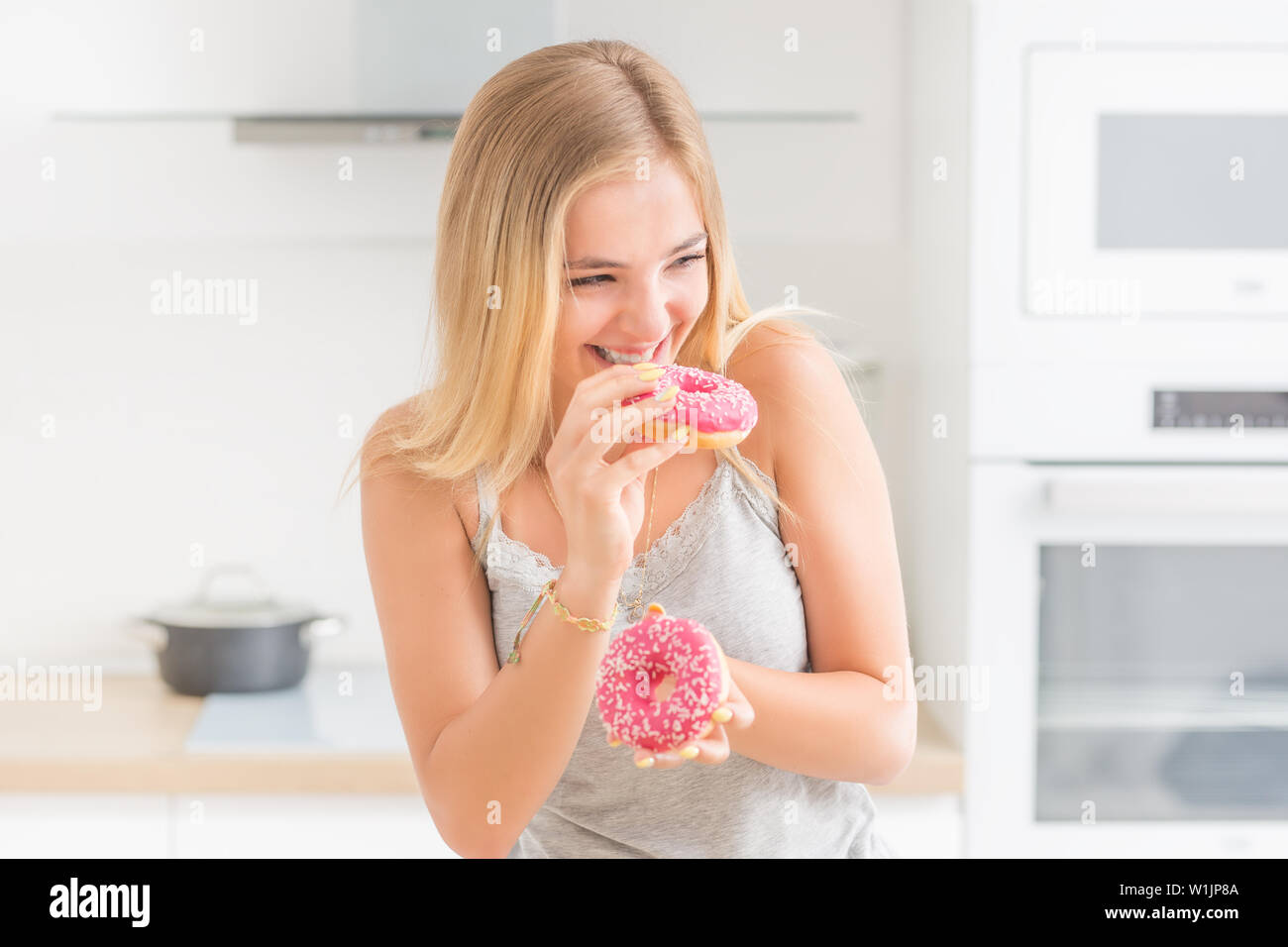 Junge blonde Mädchen isst Rosa donuts Home Küche mit Geschmack Emotionen. Stockfoto