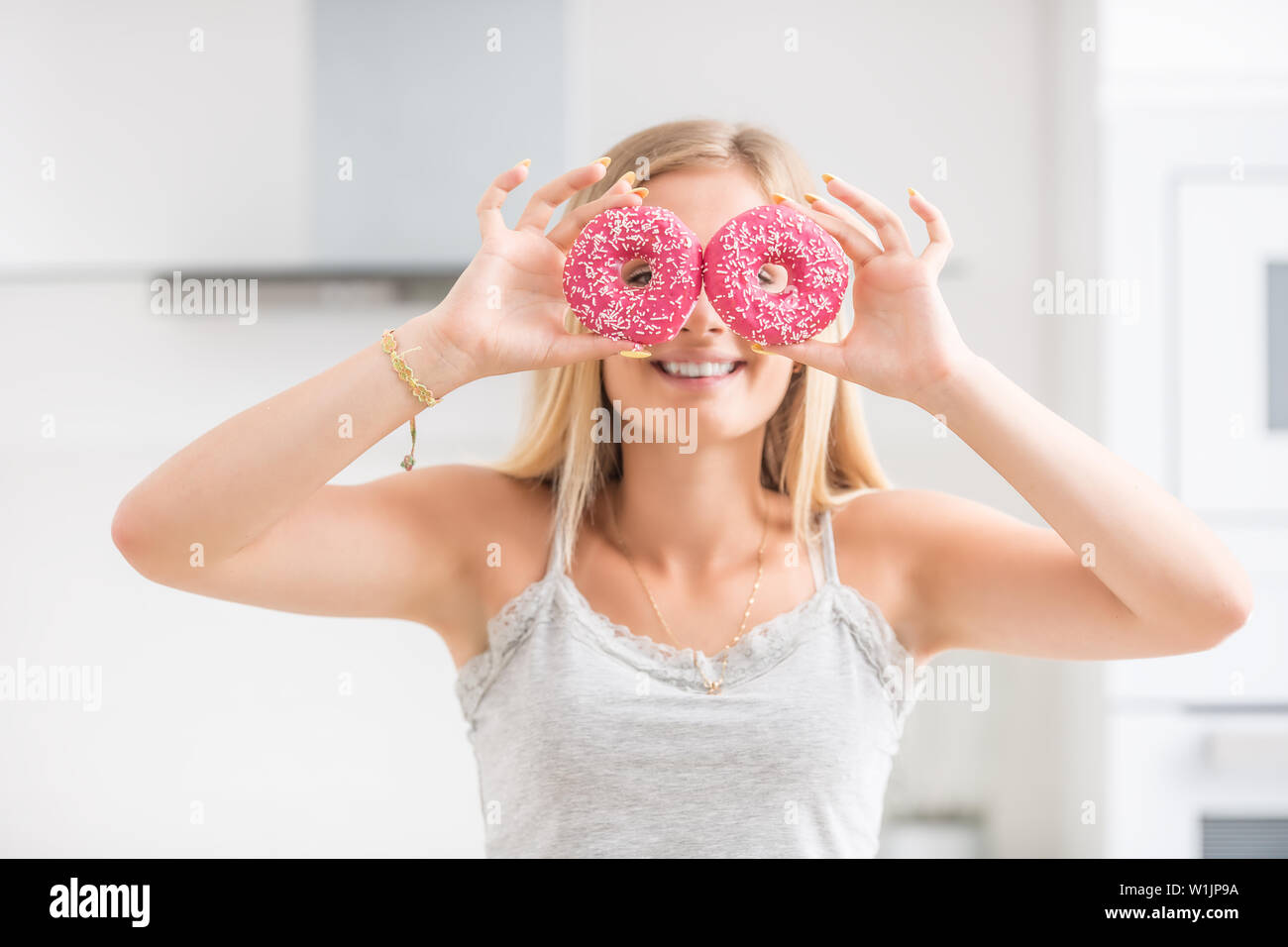 Junge Mädchen bedeckte ihr Gesicht mit rosa Donuts in der Küche zu Hause. Emotion morgen beim Frühstück. Stockfoto