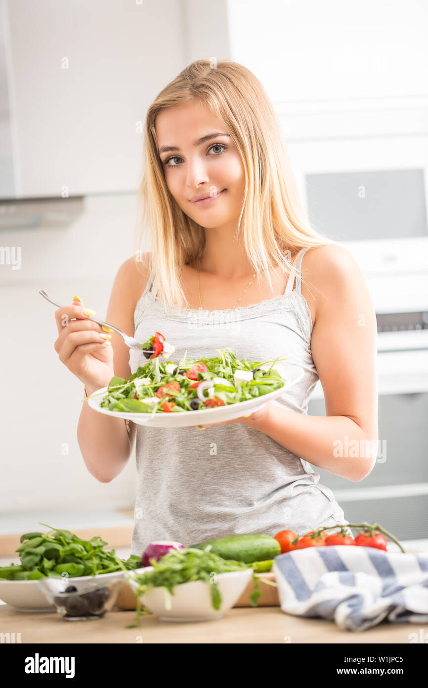 Junge blonde Mädchen glücklich gesund essen Salat aus Rucola Spinat Tomaten, Zwiebeln, Oliven und Olivenöl. Stockfoto