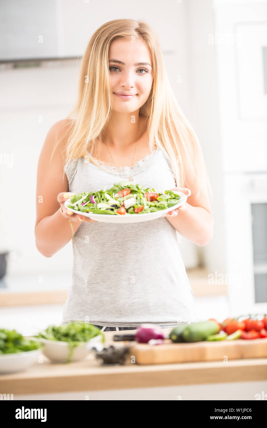 Junge blonde Mädchen glücklich gesund essen Salat aus Rucola Spinat Tomaten, Zwiebeln, Oliven und Olivenöl. Stockfoto