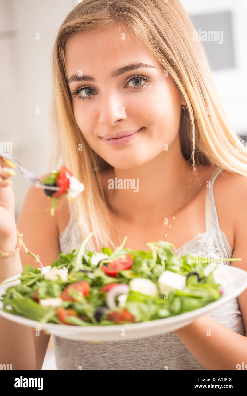 Junge blonde Mädchen glücklich gesund essen Salat aus Rucola Spinat Tomaten, Zwiebeln, Oliven und Olivenöl. Stockfoto