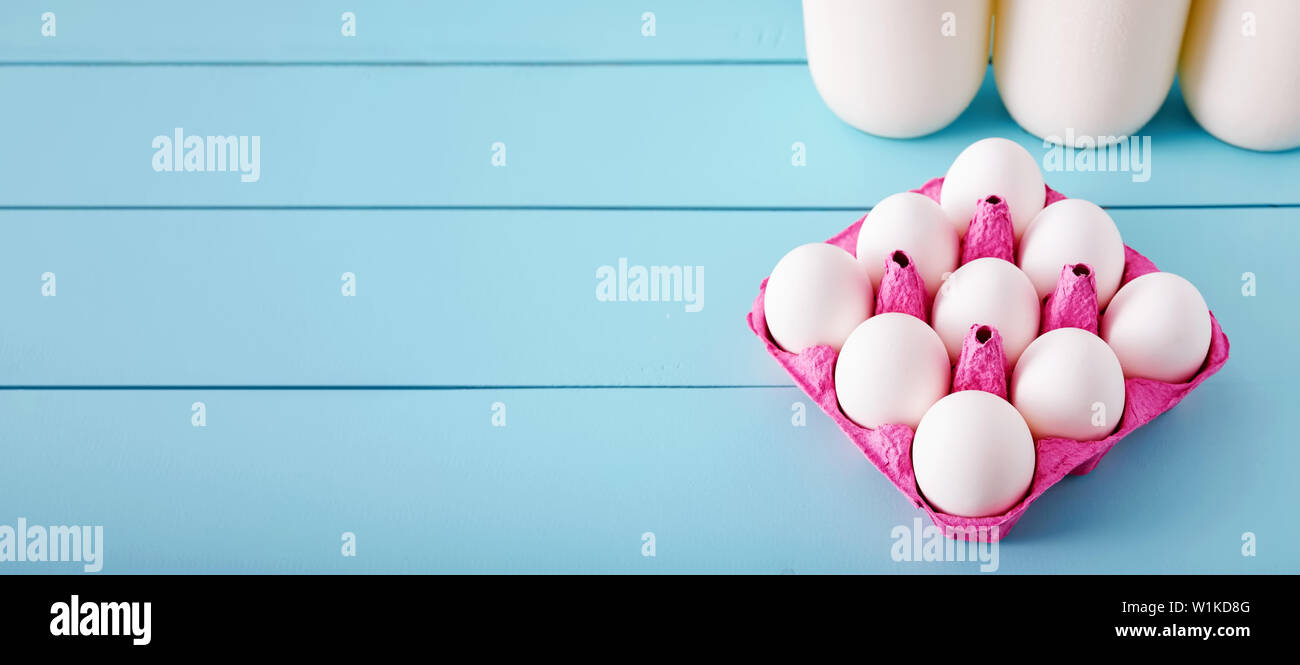 Weiße Eier in einem rosa Füller und Milchflaschen auf Türkis Holz- land Küchentisch. Banner mit Kopie Raum Stockfoto