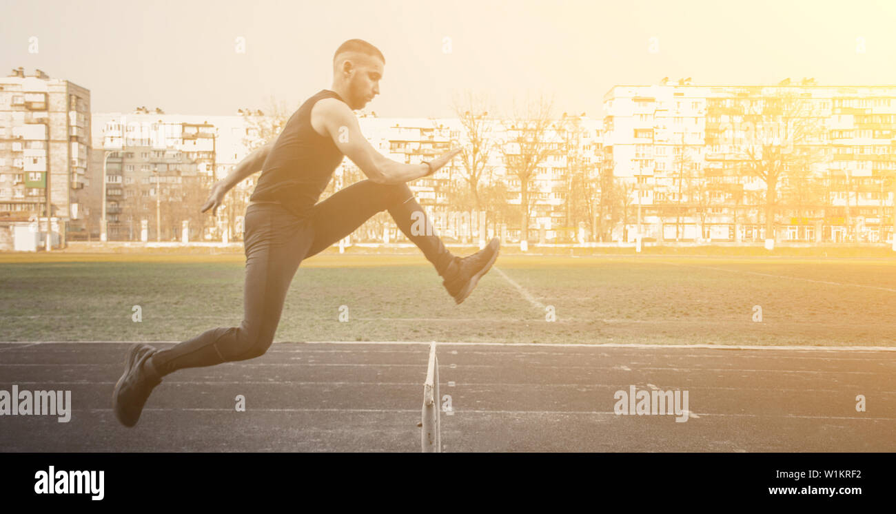 Ein Kaukasier Männlich in einem Sprung über ein Hindernis. läuft auf das Stadion. Leichtathletik Läufer in Sport einheitliche im Flug. energetischen körperlichen Aktivitäten. Stockfoto