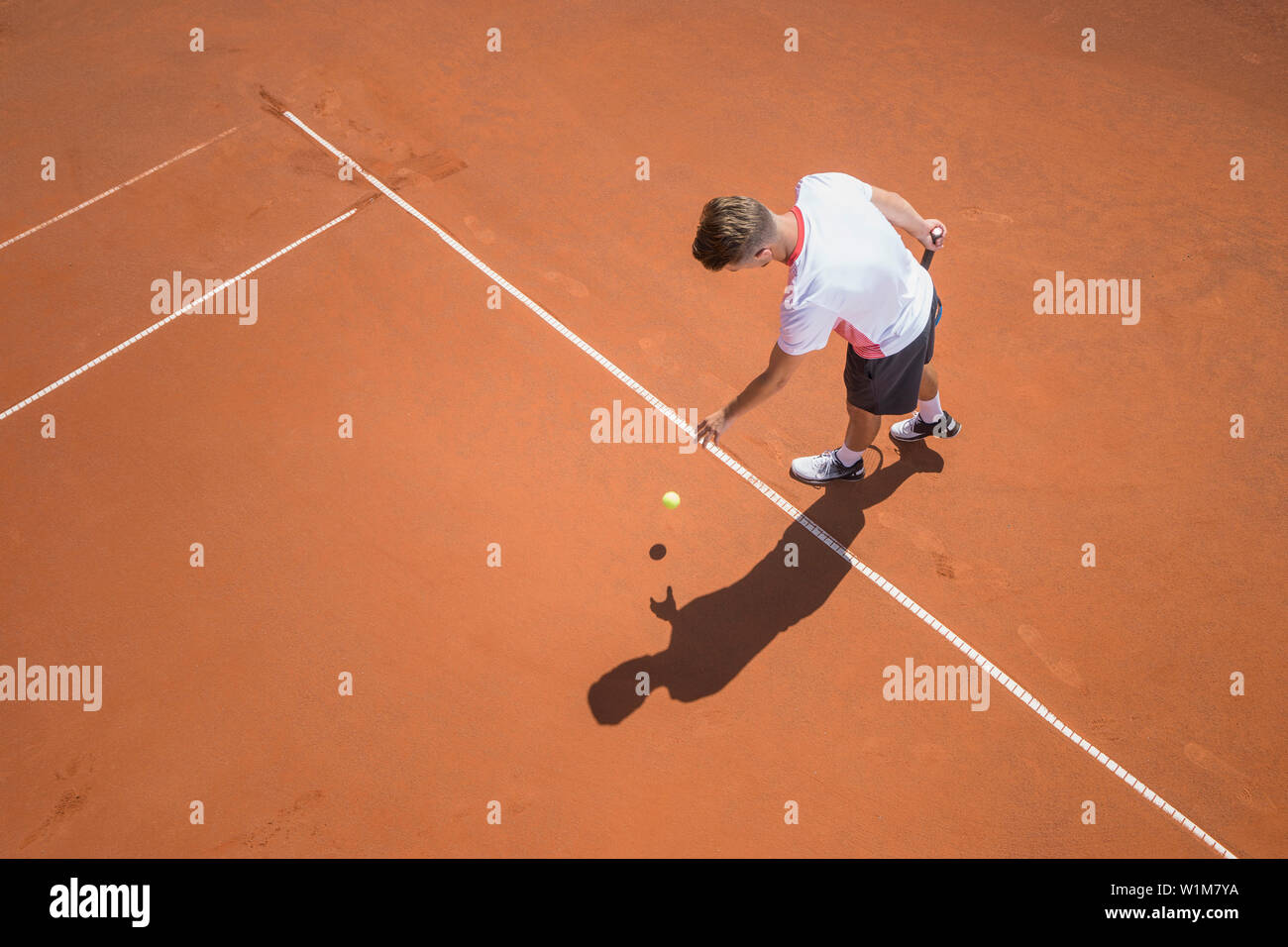 Jungen männlichen Tennisspieler vorbereiten, die Kugel auf Sunny Red Tennisplatz zu dienen, Bayern, Deutschland Stockfoto