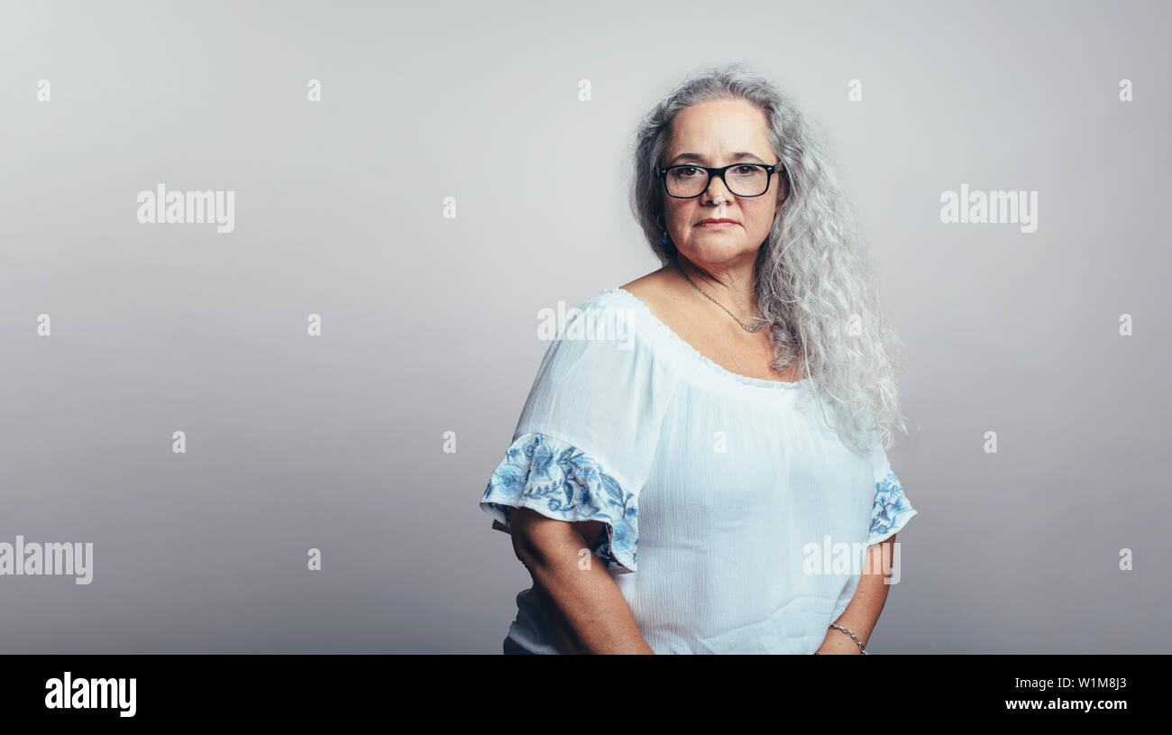 Ältere Frau in Brillen bei Kamera schaut. Alte Frau in weißen Haar auf einem grauen Hintergrund. Stockfoto