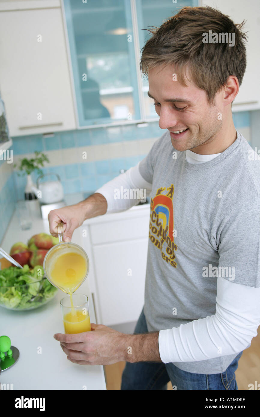 Junger Mann, gießen ein Glas Orangensaft, München, Deutschland Stockfoto