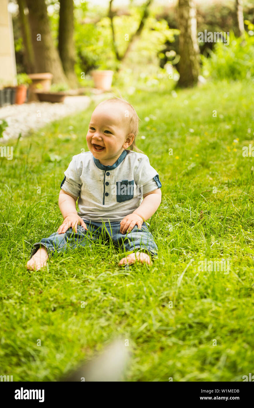 Lachendes Baby Junge sitzt auf der Wiese im Garten Stockfoto