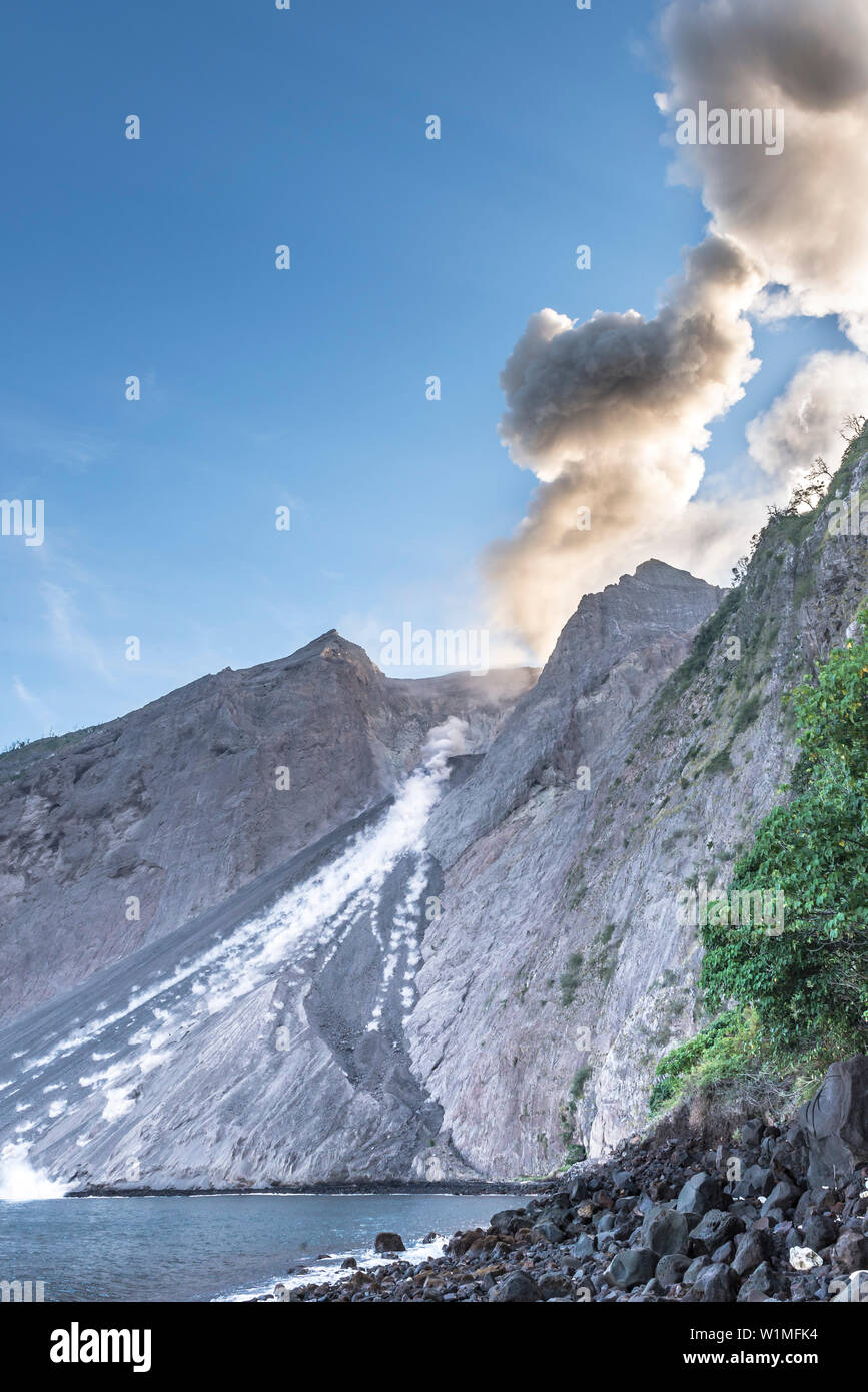 Grosse Ascheeruption mit auswürfen von Felsen am brennenden Rand von Batu Tara in der Flores See mit Leuchtdioden vulkanische Gase und Asche mit blauem Himmel. Ston Stockfoto