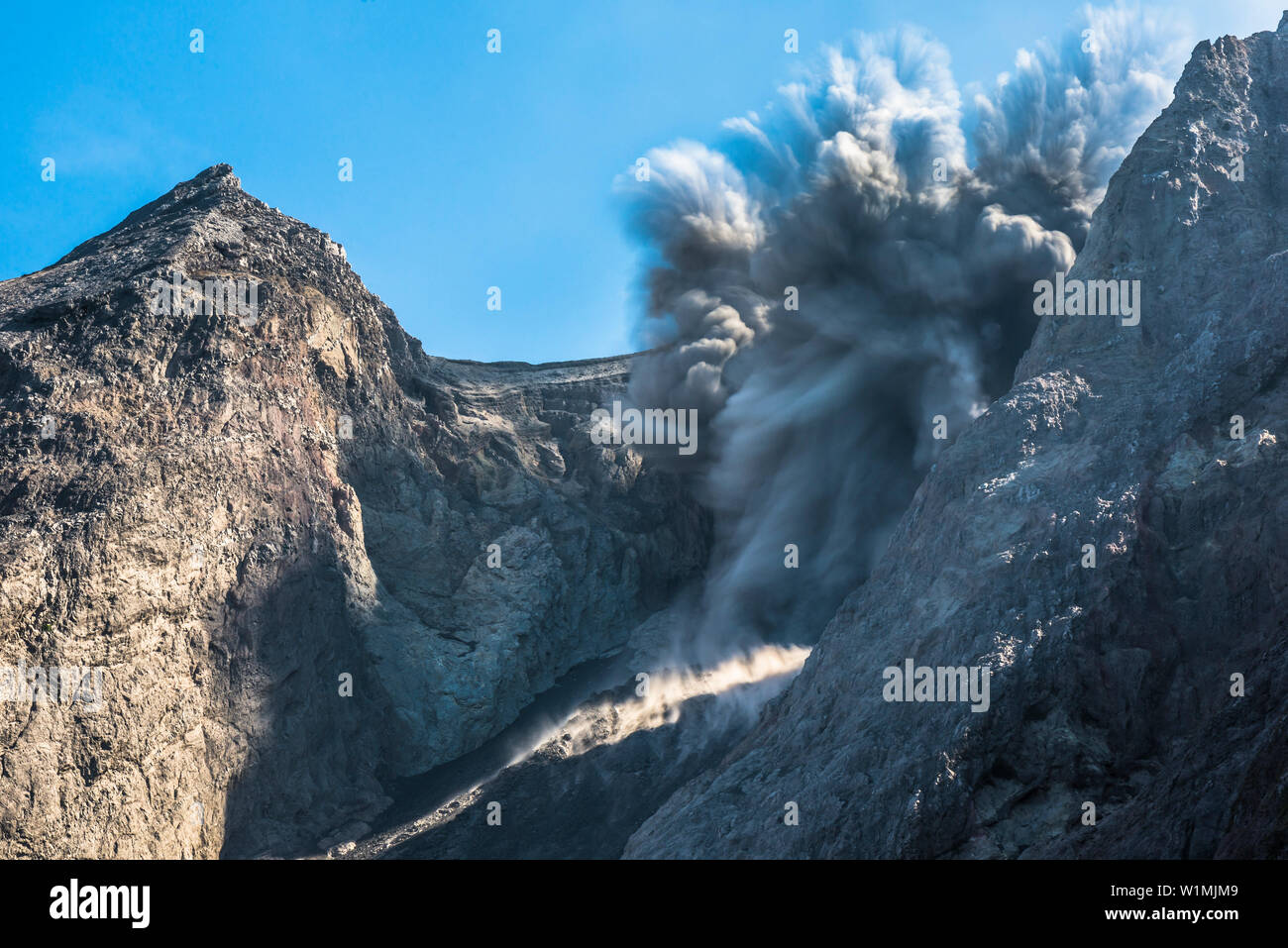 Grosse Ascheeruption mit auswürfen von Felsen am brennenden Rand von Batu Tara in der Flores See mit Leuchtdioden vulkanische Gase und Asche und blauer Himmel. Stony Stockfoto