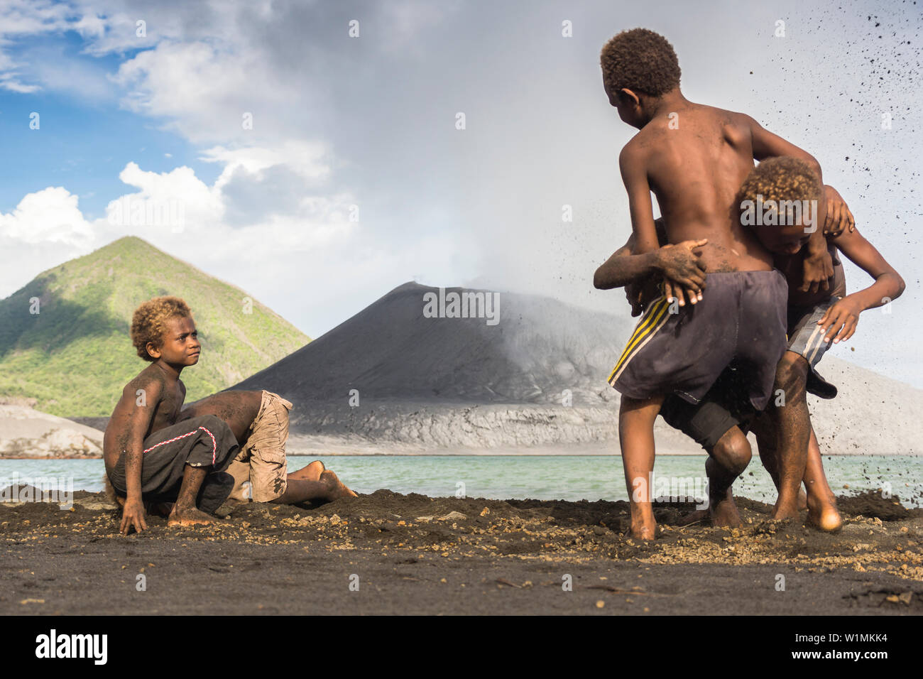 Kinder spielen im Sand während einer Eruption. Hinter ihnen die aktiven Vulkan Tavurvur, die am Meer gelegen ist. Im Hintergrund die Grüne Stockfoto