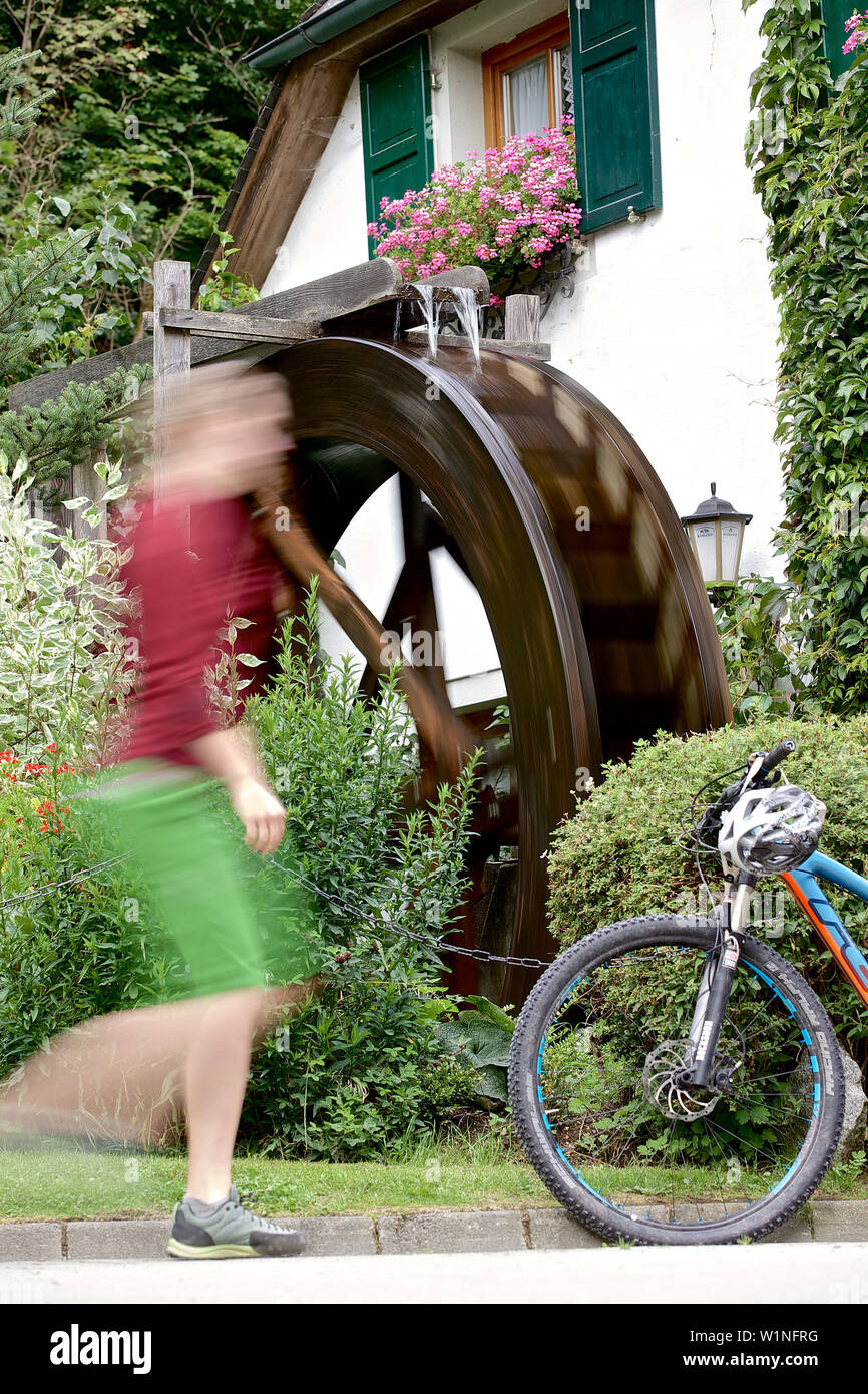 Junge Frau zu Fuß zu Ihrem Fahrrad an ein altes Wasserrad Stockfoto