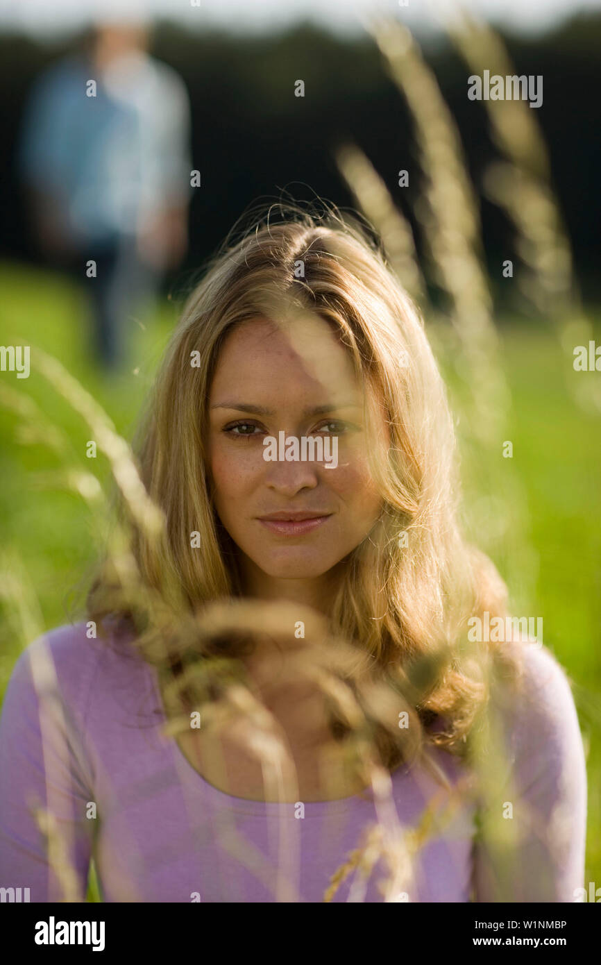 Junge Frau sitzt auf der Wiese, nicht erkennbare Person im Hintergrund Stockfoto