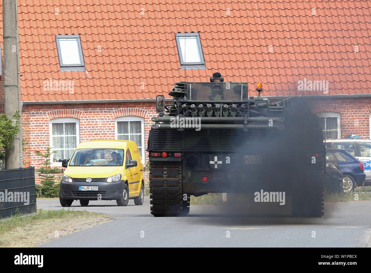 Trebs, Deutschland. 03 Juli, 2019. Eine Bundeswehr Chain Mail Tank und eine Deutsche Post Auto pass Miteinander in der Stadt Trebs. Die Situation im Wald Feuer auf einem ehemaligen Truppenübungsplatz in der Nähe von Lübtheen in Mecklenburg-Vorpommern hat sich zum ersten Mal seit dem Ausbruch des Feuers gelockert. Die ersten Bewohner waren in der Lage, ihre Häuser, die vorsorglich geräumt worden war. Credit: Bodo Marks/dpa/Alamy leben Nachrichten Stockfoto