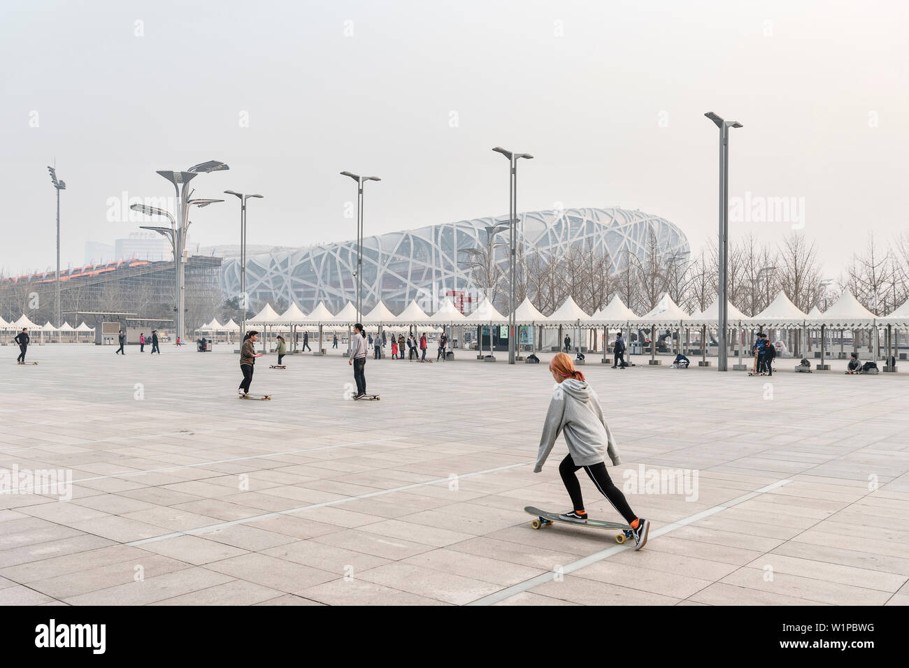 Chinesische Jugend mit longboards vor der sogenannten Bird's Nest von Herzog & de Meuron, National Stadium, starke Luftverschmutzung, Olympic Green, Peking, Stockfoto