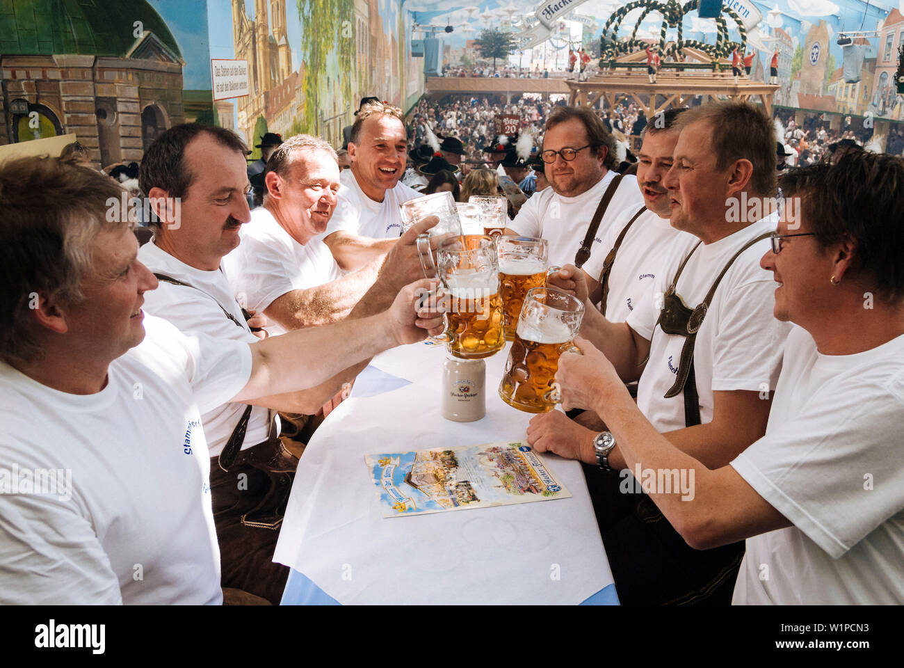 Männer im mittleren Alter heben ihr Bier mugsto Toast auf dem Oktoberfest, München, Bayern, Deutschland Stockfoto
