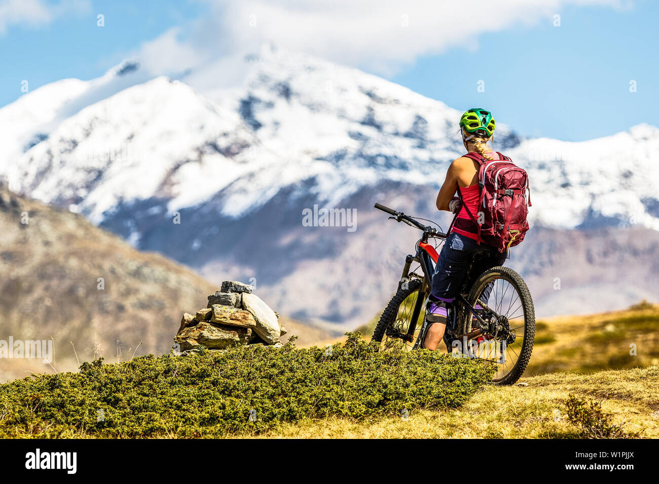 Junge Frau nimmt eine Pause auf Ihrem Mountainbike und genießt die Aussicht auf die Ortlergruppe, Bormio, Sondrino, Lombardei, Südtirol, Italien Stockfoto
