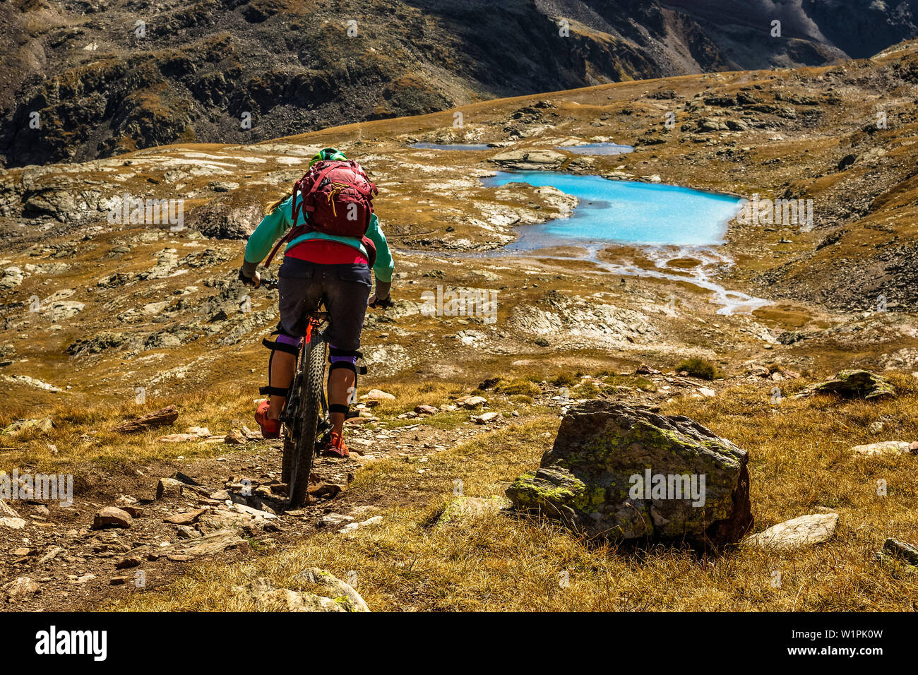 Junge Frau reitet Ihr Mountainbike auf einem Singletrail, Richtung einer türkisblauen Bergsee, Bormio, Lombardei, Südtirol, Italien Stockfoto