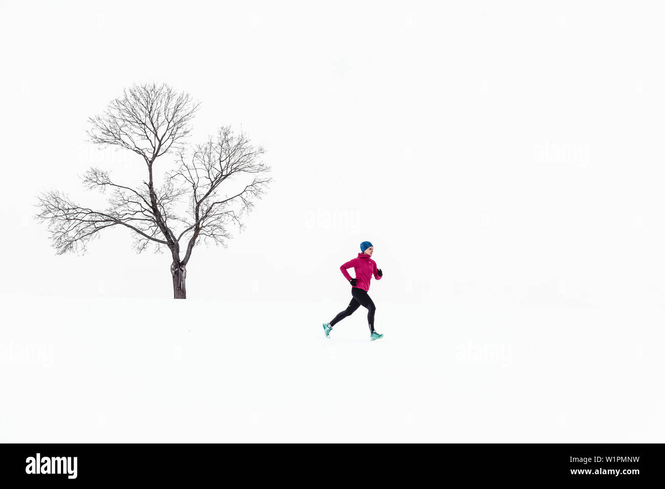 Junge Frau läuft auf schneebedeckten Feld in Berg, Starnberger See, Bayern, Deutschland. Stockfoto