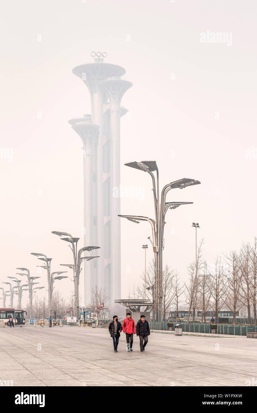 Chinesische Männer (einige mit Maske) Spaziergang durch den Park, Olympic Tower in starke Luftverschmutzung im Hintergrund gewickelt, Olympic Green, Peking, China, Asien Stockfoto