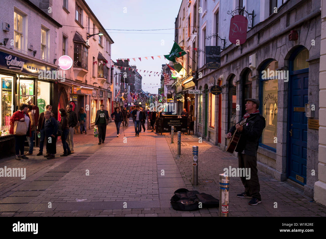 Ein strassenmusiker spielt Gitarre und singt, während Quay Street mit Fußgängern vorbei auf dem Weg zu ihren Nacht heraus, füllt, Grafschaft Galway Galw Stockfoto